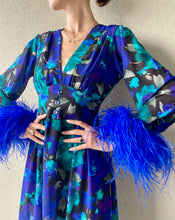 Carica l'immagine nel visualizzatore di Gallery, Abito maxi manica lunga elasticizzato in vita e bottoncini stile corsetto. Fantasia blu floreale, con boa in piuma di struzzo blu elettrico ai polsi. Spacco laterale. Attaccatura del boa tramite asoline e bottoncini cuciti a mano, per facilitare il lavaggio e per poterlo utilizzare anche senza piuma. Composizione tessuto: 50% polyester; 45% viscose; 5% elastam.