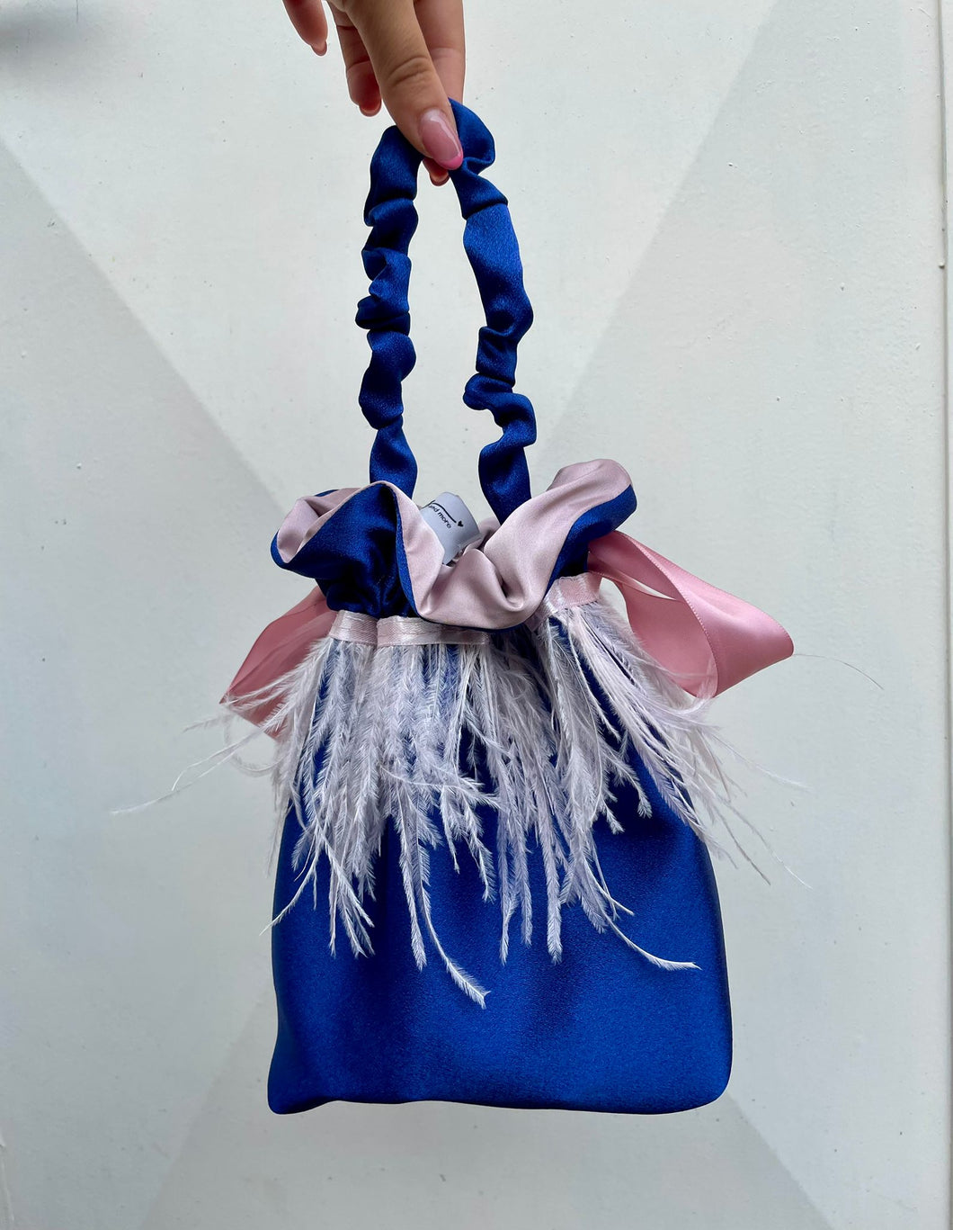 Borsetta midi blu handmade in raso esterno con giro di piume di struzzo rosa cucito a mano e raso interno rosa; chiusura in raso con fiocco e manico arricciato. Perfetta per completare il tuo outfit da cerimonia. 