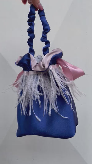 Borsetta midi blu handmade in raso esterno con giro di piume di struzzo rosa cucito a mano e raso interno rosa; chiusura in raso con fiocco e manico arricciato. Perfetta per completare il tuo outfit da cerimonia. 